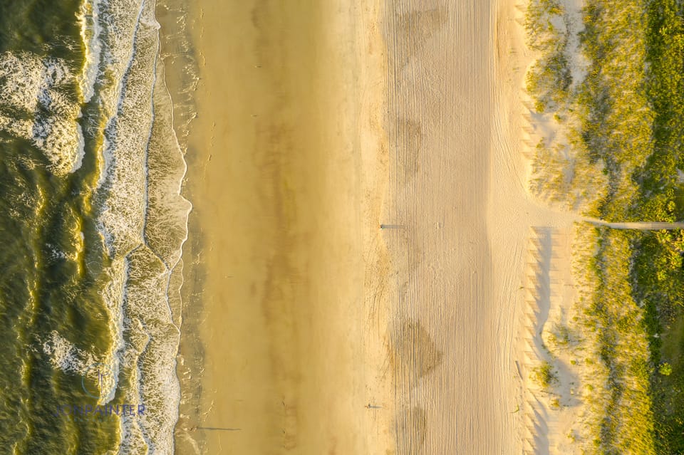 This is a drone photo looking down. A few early-risers enjoy the sunrise as waves wash on the golden shore.