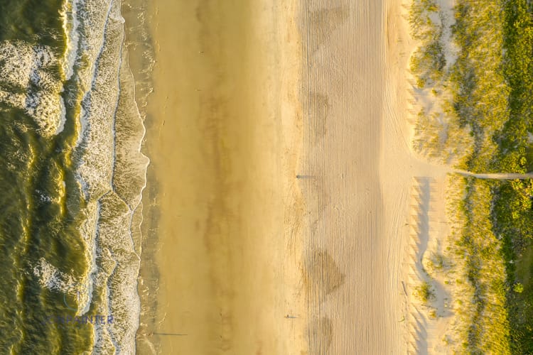 This is a drone photo looking down. A few early-risers enjoy the sunrise as waves wash on the golden shore.